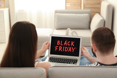 Couple using laptop with Black Friday announcement on screen at home