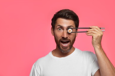Funny man hiding his eye with tasty sushi roll on pink background. Space for text