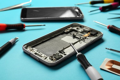 Damaged smartphone and repair tools on light blue background, closeup