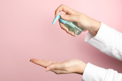 Woman applying antiseptic gel on hand against pink background, closeup