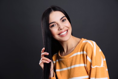 Portrait of happy young woman with beautiful black hair and charming smile on dark background
