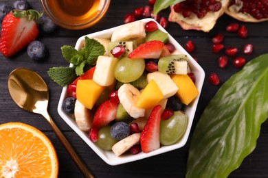 Delicious fresh fruit salad in bowl on black wooden table, flat lay