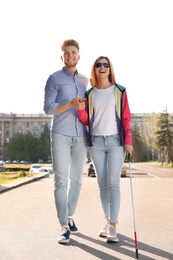 Photo of Young man helping blind person with long cane walking outdoors