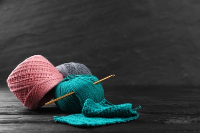 Clews of colorful knitting threads and crochet hook on black wooden table, space for text