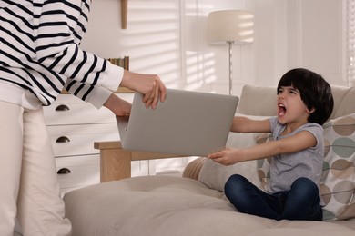 Photo of Internet addiction. Woman taking laptop from her angry son in living room