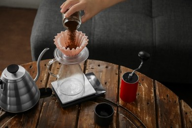Barista putting coffee into jug with wave dripper at wooden table in cafe, closeup