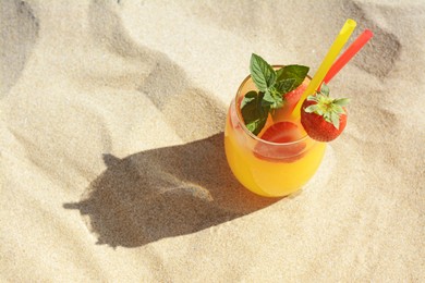 Glass of refreshing drink with strawberry on sandy beach, above view. Space for text