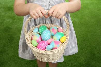 Little girl with basket full of Easter eggs on green grass, closeup