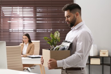 Upset dismissed man carrying box with personal stuff in office