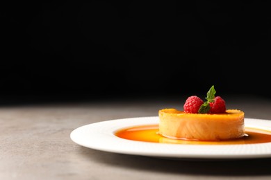 Delicious pudding with caramel and raspberries on grey table against black background. Space for text