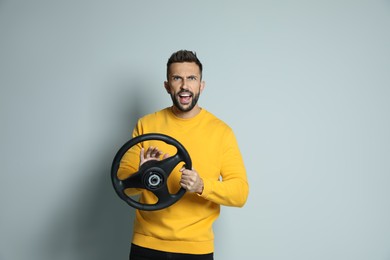 Emotional man with steering wheel on grey background