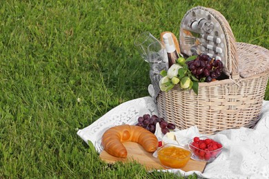 Picnic blanket with tasty food, flowers, basket and cider on green grass outdoors. Space for text