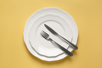 Photo of Clean plates with shiny silver cutlery on yellow background, flat lay