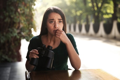 Jealous woman with binoculars spying on ex boyfriend in outdoor cafe