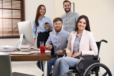 Young woman in wheelchair with colleagues at workplace