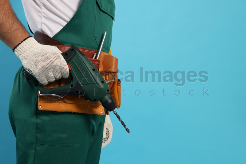 Worker in uniform with power drill on light blue background, closeup. Space for text