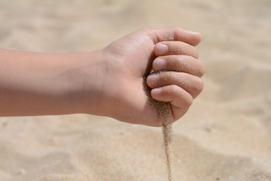 Child pouring sand from hand outdoors, closeup. Fleeting time concept