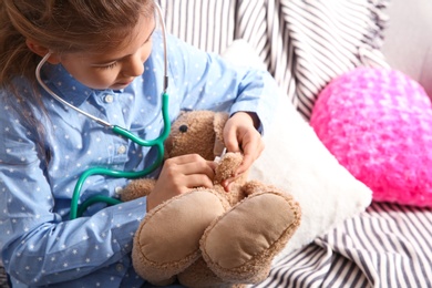 Cute child imagining herself doctor while playing with stethoscope on sofa in living room