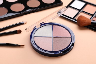 Photo of Colorful contouring palettes with brushes on beige background, closeup. Professional cosmetic product