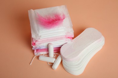 Menstrual pads with pink feather and other period products on pale orange background