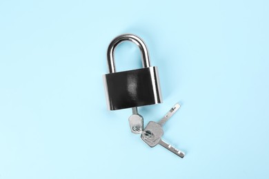 Modern padlock with keys on light blue background, top view