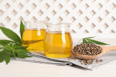 Hemp oil, fresh leaves and seeds on white wooden table