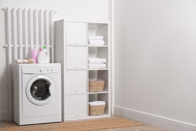 Photo of Laundry room interior with modern washing machine and shelving unit near white wall