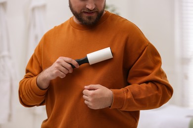 Photo of Man cleaning clothes with lint roller at home, closeup