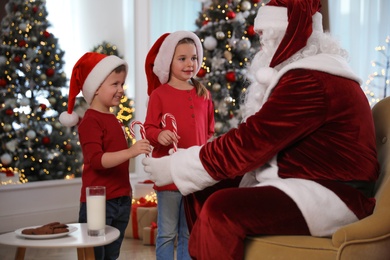 Santa Claus giving candy canes to children in room decorated for Christmas