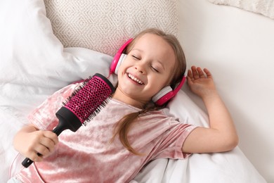 Cute little girl in headphones with hairbrush singing on bed