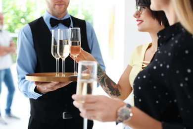 Waiter serving champagne to women at exhibition in art gallery