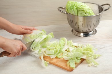 Photo of Woman cutting Chinese cabbage at white wooden kitchen table, closeup