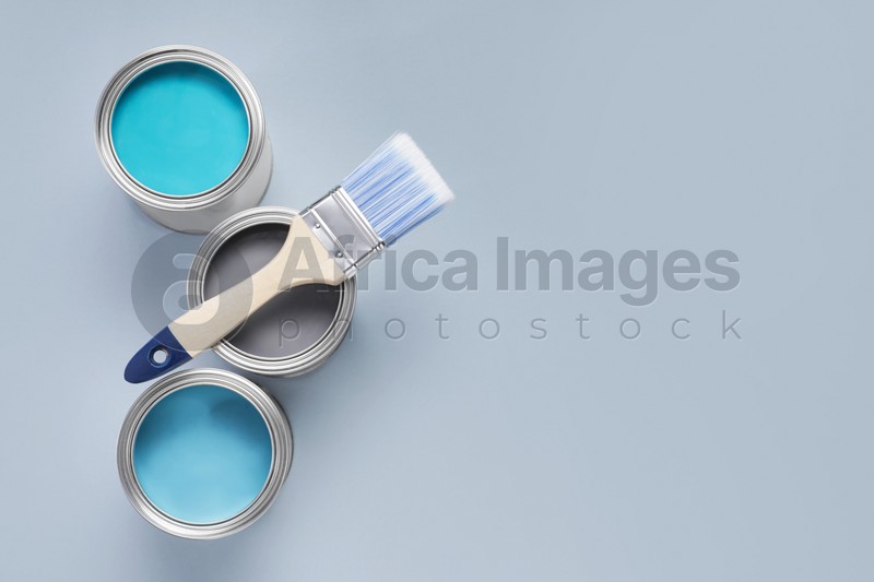 Photo of Cans with different paints and brush on light background, flat lay. Space for text