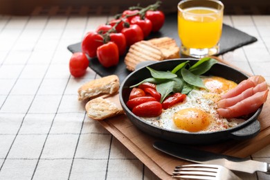 Delicious fried eggs with spinach, tomatoes and ham served on table. Space for text