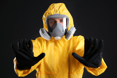 Man in chemical protective suit making stop gesture on black background. Virus research