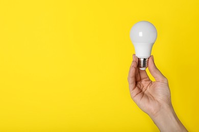 Woman holding LED light bulb on yellow background, closeup. Space for text