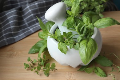 Photo of Mortar with different fresh herbs on wooden table, closeup