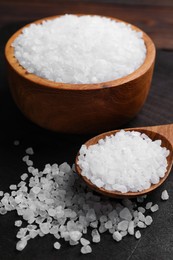 Spoon and bowl of natural sea salt on wooden table, closeup