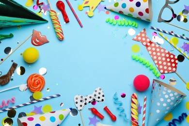 Frame of party hats and other festive items on light blue background, flat lay with space for text. Birthday surprise