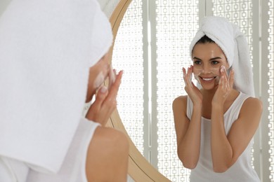Happy young woman applying cleansing foam onto face near mirror in bathroom