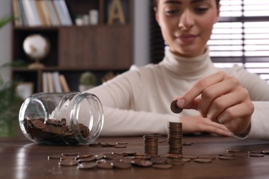 Woman stacking coins at wooden table indoors, closeup