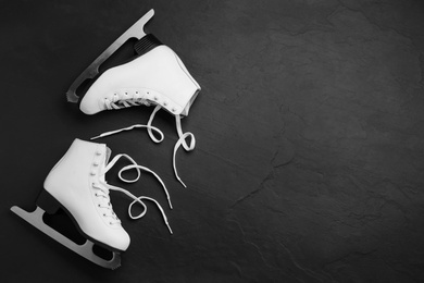Pair of white ice skates on black stone background, top view. Space for text