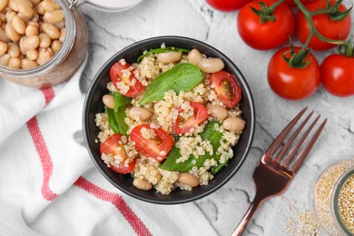 Photo of Delicious quinoa salad with tomatoes, beans and spinach leaves served on white textured table, flat lay