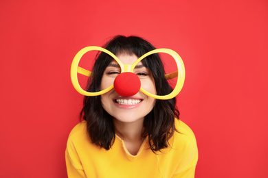 Joyful woman with large glasses and clown nose on red background. April fool's day