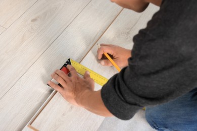 Photo of Professional worker using ruler during installation of laminate flooring, closeup