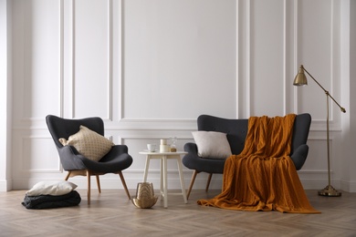 Comfortable sofa with knitted blanket, armchair and lamp in stylish room interior