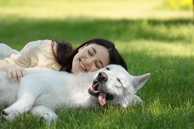 Teenage girl lying with her white Swiss Shepherd dog on green grass in park