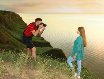 Male photographer taking picture of young woman with professional camera on green hill