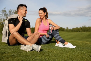 Man and woman in fitness clothes resting on green grass outdoors