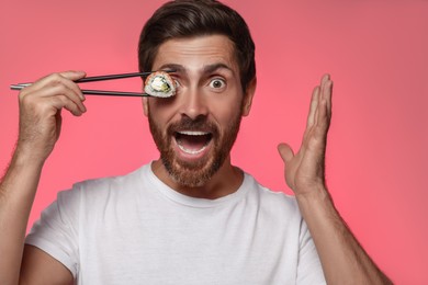 Photo of Emotional man hiding his eye with tasty sushi roll against pink background